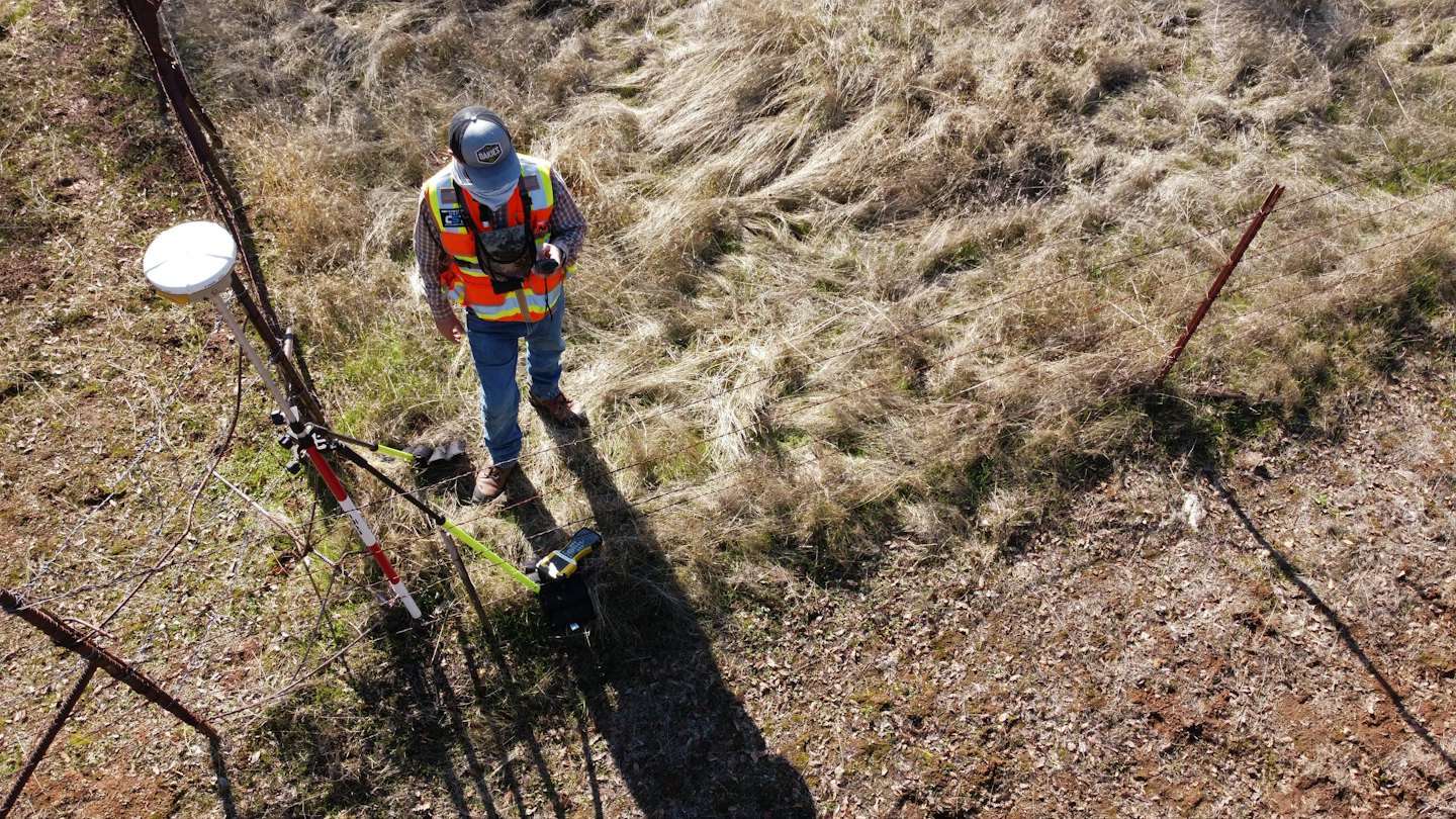 Surveyor operates equipment in a sunny, grassy field.
