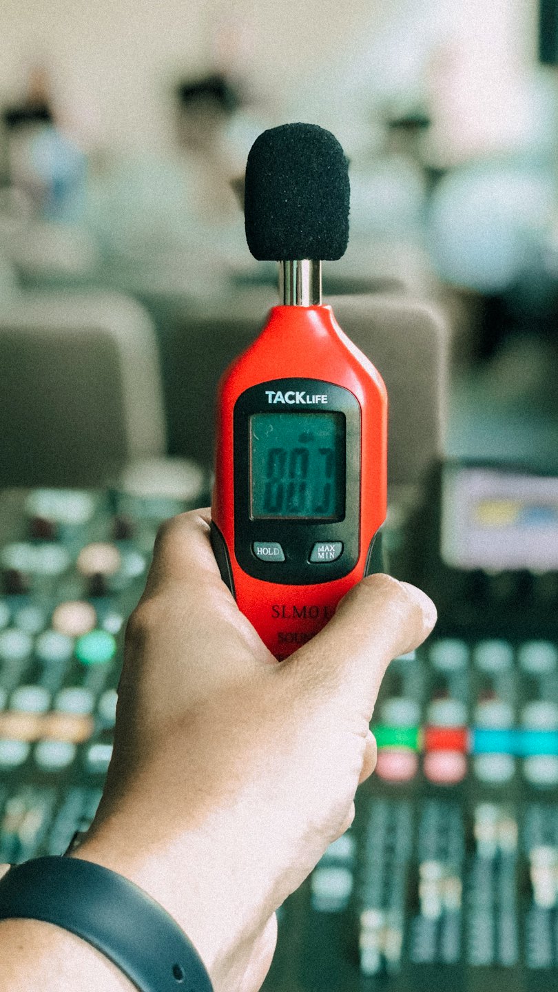 A hand holds a sound level meter displaying a measurement.